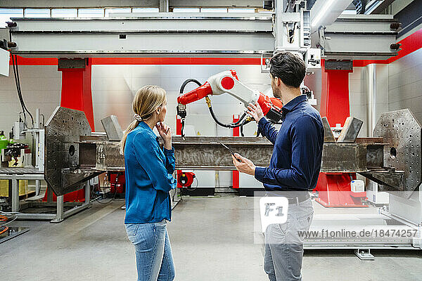 Engineer explaining robots to colleague standing in factory