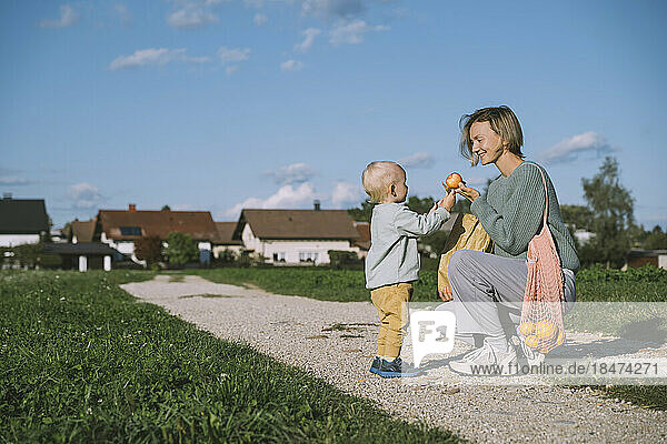 Lächelnde Frau gibt ihrem Sohn auf dem Fußweg einen Apfel