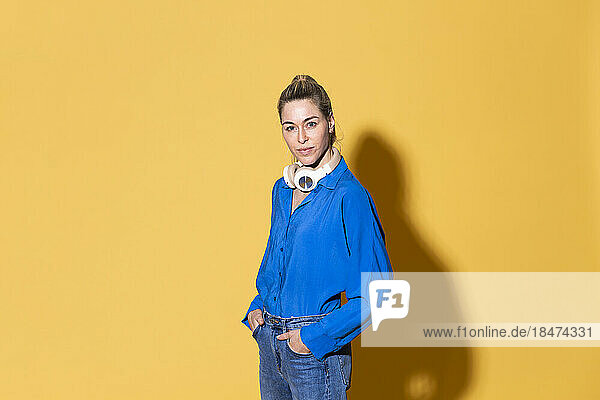Woman with hands in pockets against yellow background