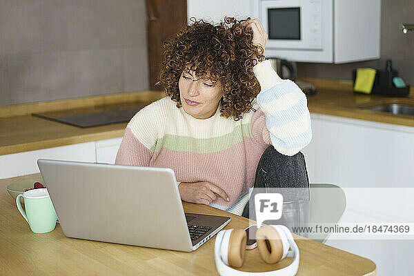 Lächelnder Freiberufler mit dem Kopf in der Hand  der zu Hause einen Laptop benutzt