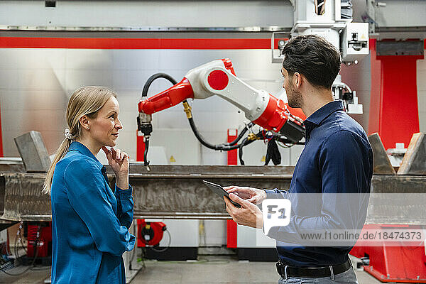 Mature engineer looking at technician holding tablet PC in robot factory