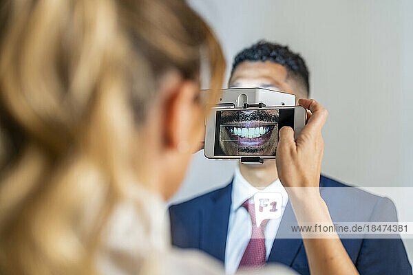 Geschäftsfrau fotografiert mit Vergrößerungsgerät das Lächeln eines Kollegen per Mobiltelefon