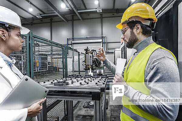 Engineer with colleague wearing hardhat having discussion in factory