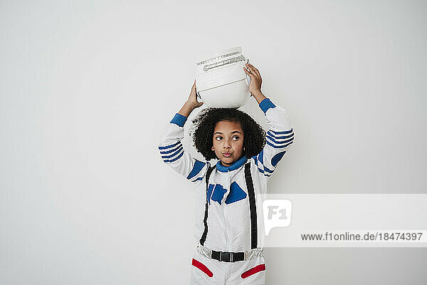 Girl holding space helmet on head in front of white wall