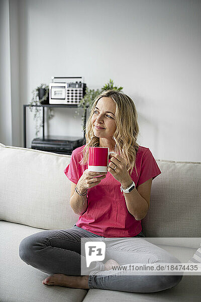 Nachdenkliche reife Frau sitzt mit einer Kaffeetasse zu Hause