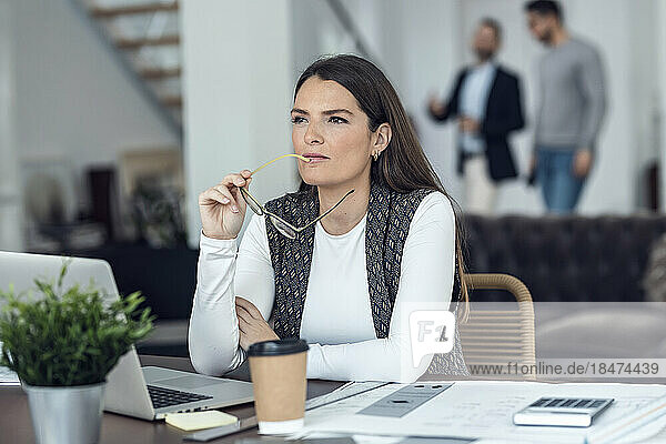 Nachdenkliche Geschäftsfrau mit Brille sitzt am Schreibtisch