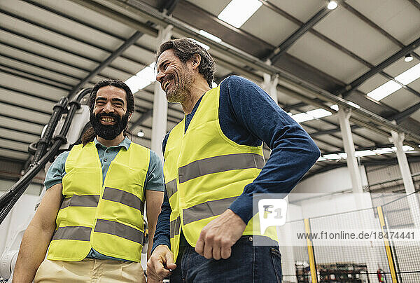 Happy engineers wearing reflective clothing standing in robotics factory