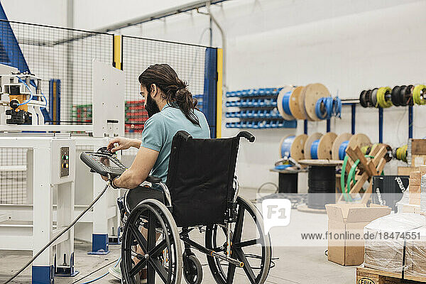Engineer sitting in wheelchair using control panel at factory