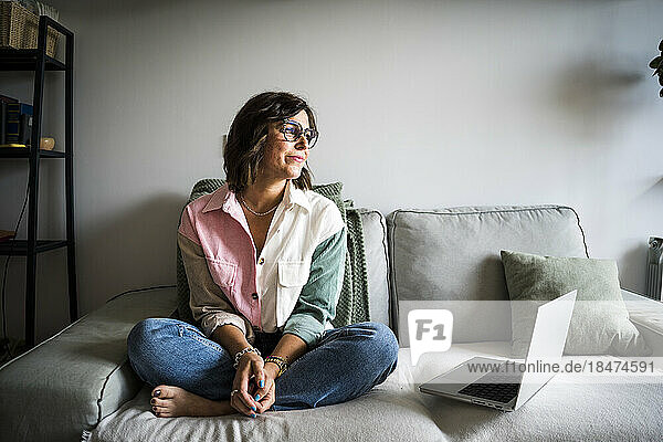 Nachdenkliche Frau mit Laptop sitzt auf dem Sofa
