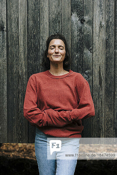 Smiling woman with eyes closed leaning on wooden wall