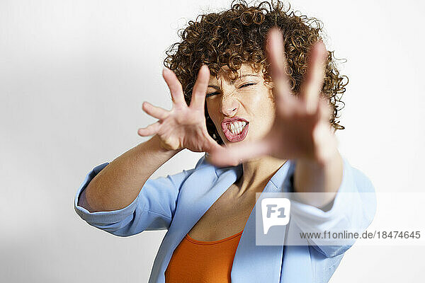 Woman with curly hair making face and gesturing against white background