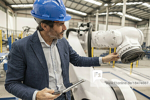 Engineer with tablet PC examining robotics part in factory