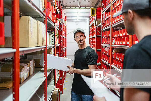Warehouse worker holding box by colleague taking inventory at factory