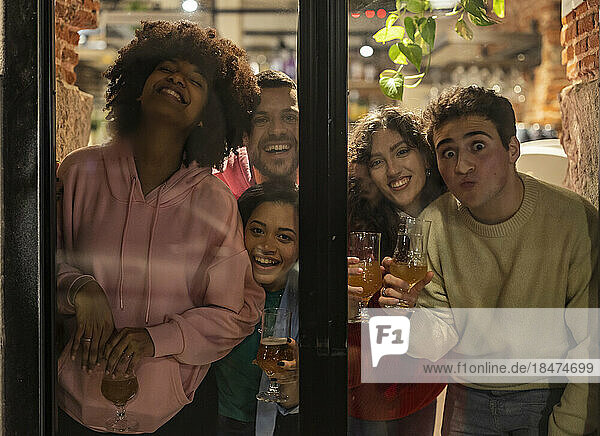 Young friends holding drinks having fun seen through glass