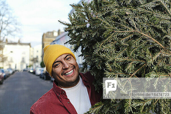 Happy man carrying Christmas tree on street