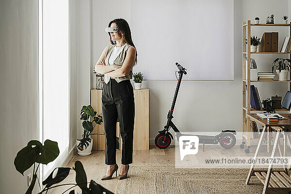 Businesswoman wearing VR glasses standing with arms crossed in office