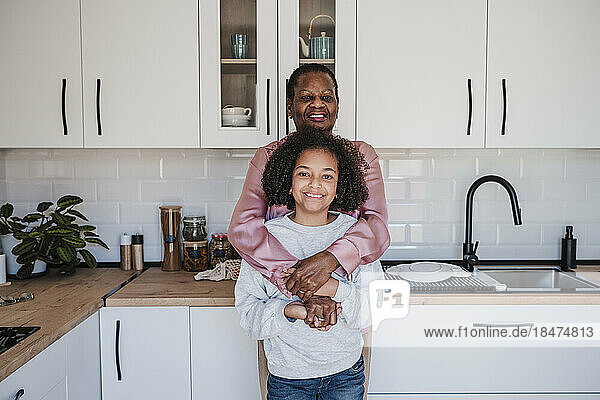 Lächelndes Mädchen steht mit Großmutter zu Hause in der Küche