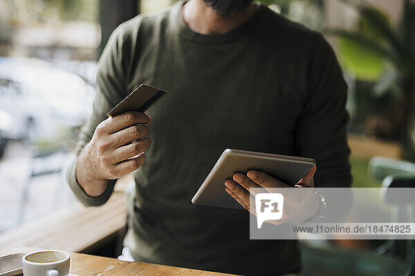 Mann mit Kreditkarte benutzt Tablet-PC im Café