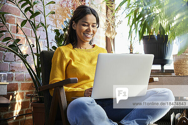 Happy woman using laptop sitting on chair at home