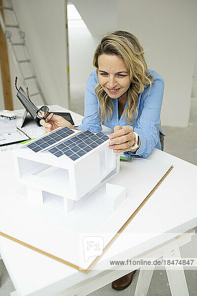 Smiling architect examining model home at desk