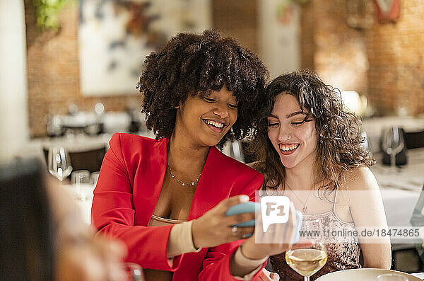 Happy woman sharing smart phone with friend at restaurant