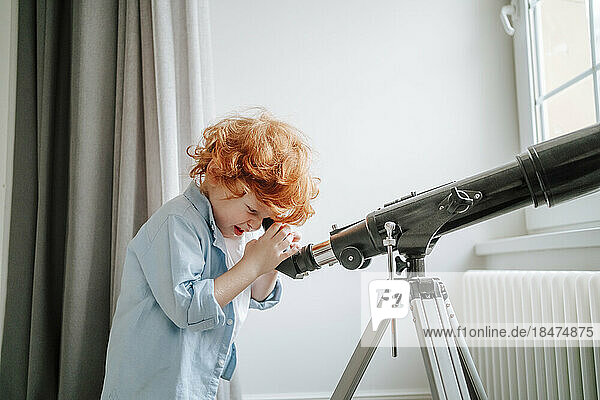 Curious boy looking through telescope at home