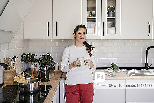 Lächelnde Frau hält Kaffeetasse in der Küche