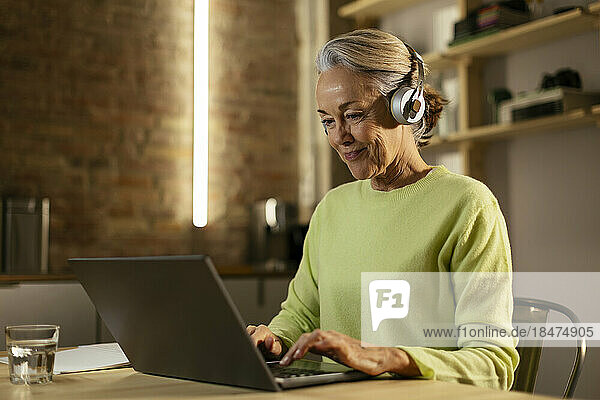 Smiling freelancer wearing wireless headphones using laptop at desk