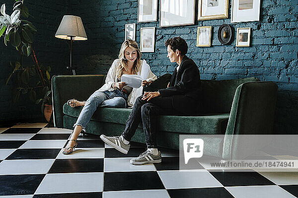 Actress reading script sitting with producer on sofa at film set