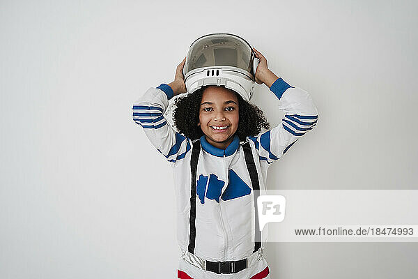 Smiling girl wearing space helmet in front of white wall
