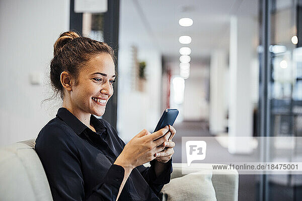 Happy businesswoman using smart phone on sofa in office