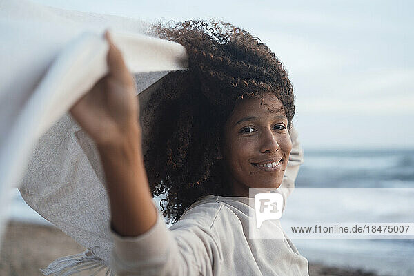 Glückliche Frau mit Schal vor dem Meer am Strand