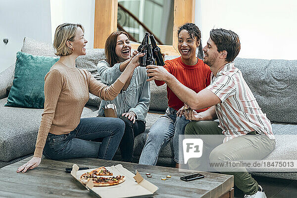 Cheerful colleagues toasting beer bottles on sofa at office