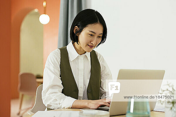 Lächelnde Geschäftsfrau mit kurzen Haaren  die im Büro am Laptop arbeitet