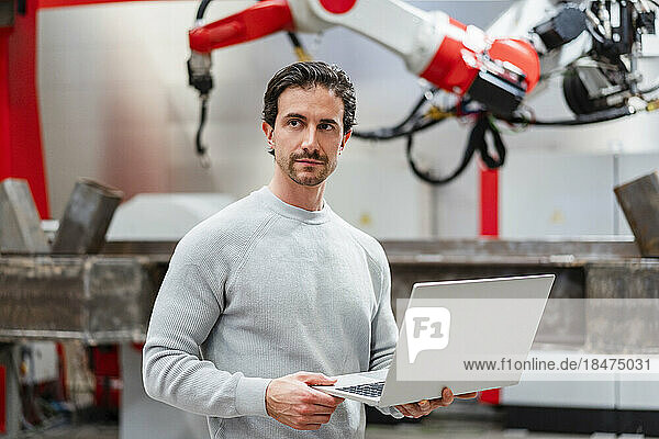 Engineer holding laptop standing in factory