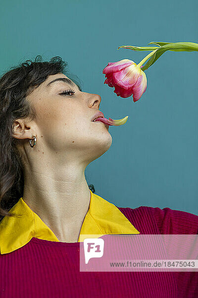 Young woman holding petal of tulip in mouth against green background
