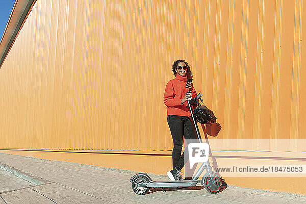 Happy woman holding smart phone standing with electric push scooter on footpath