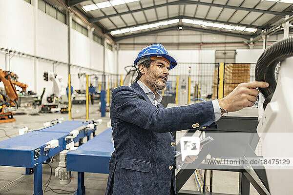 Engineer wearing hardhat examining machinery parts in factory