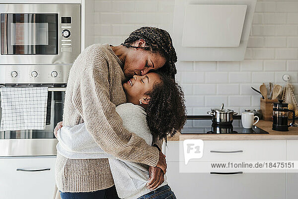 Mother kissing daughter in kitchen at home
