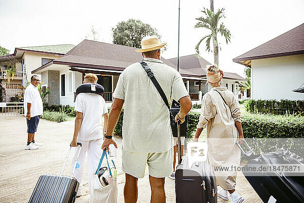 Rückansicht einer Familie  die im Urlaub mit Gepäck zur Villa läuft