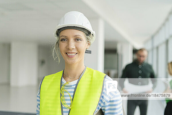 Smiling woman wearing protective workwear with colleagues in background in office