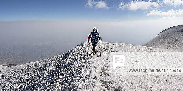 Senior woman hiking on snow covered mountain in front of sky at weekend