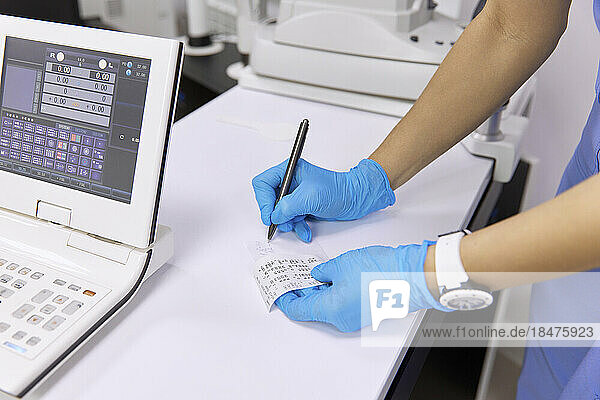 Augenarzt schreibt Testergebnisse am Schreibtisch in der Klinik auf Papier