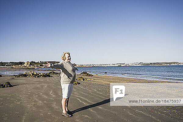 Carefree senior woman with arms outstretched standing at beach
