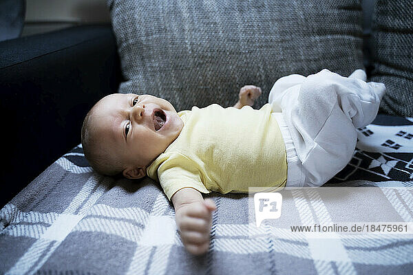 Baby boy yawning on sofa at home