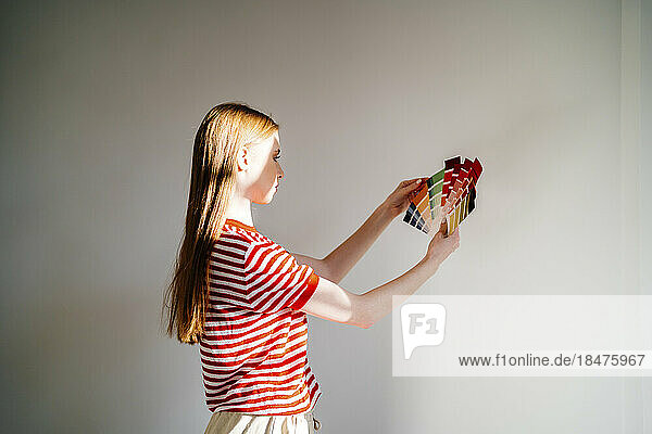 Teenage girl holding color swatch in front of white wall