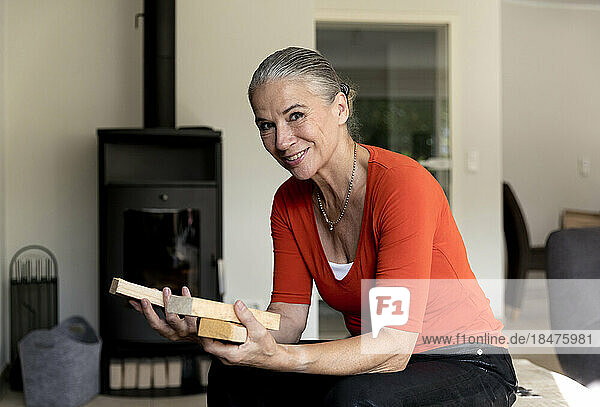 Smiling woman with firewood sitting in living room at home