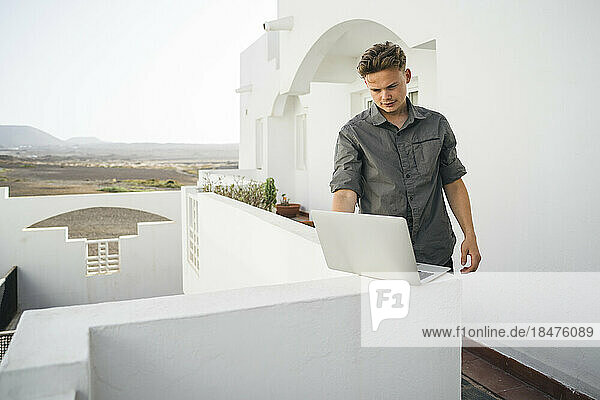 Junger Freiberufler arbeitet am Laptop auf dem Balkon