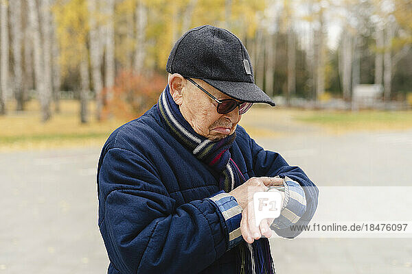 Elderly man checking time on wristwatch at park