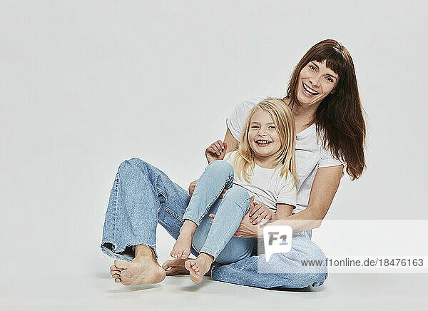 Glückliche Tochter sitzt mit Mutter vor weißem Hintergrund
